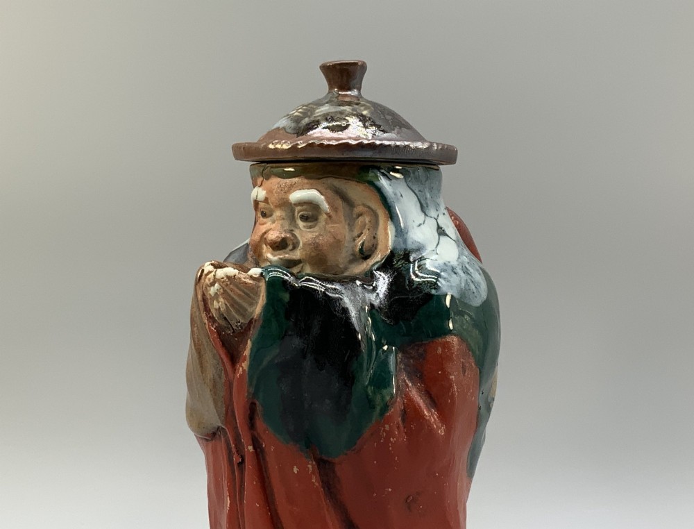 An antique Japanese Sumida Gawa lidded pottery jug sculpted in the form of a robed figure with red attire, green glaze drips, and a matching fitted lid. View VII