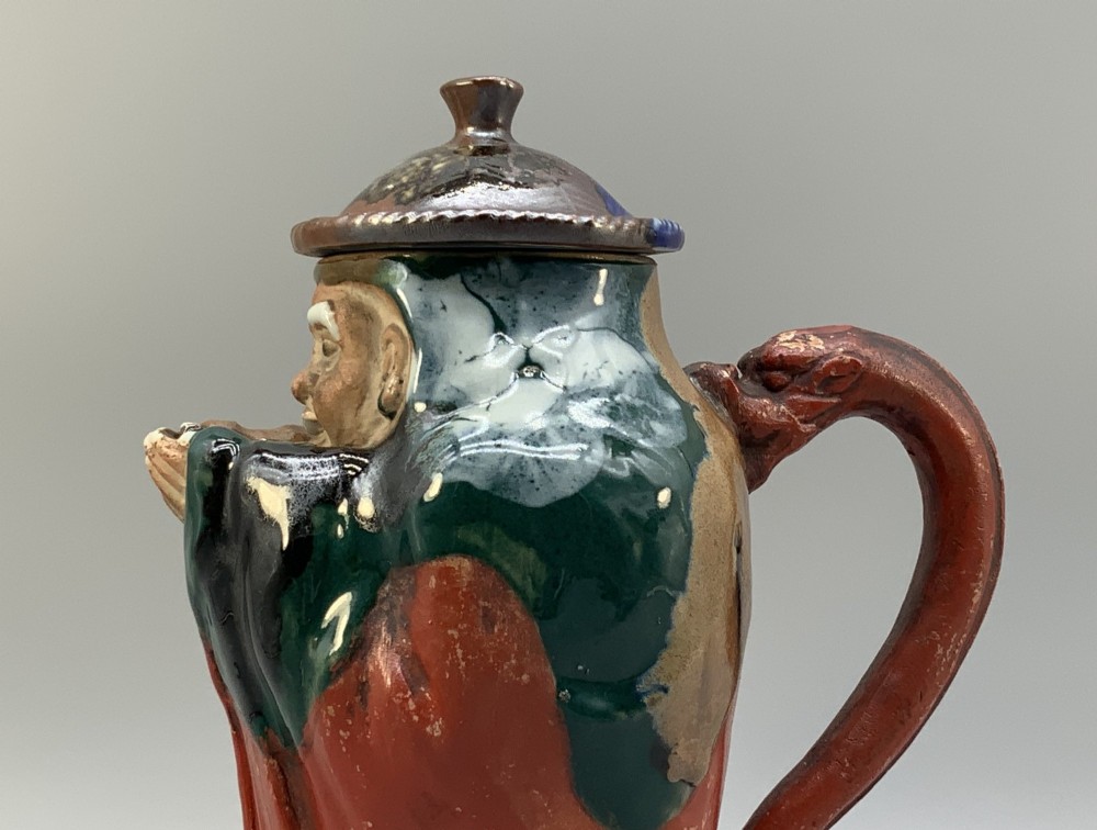 An antique Japanese Sumida Gawa lidded pottery jug sculpted in the form of a robed figure with red attire, green glaze drips, and a matching fitted lid. View VIII