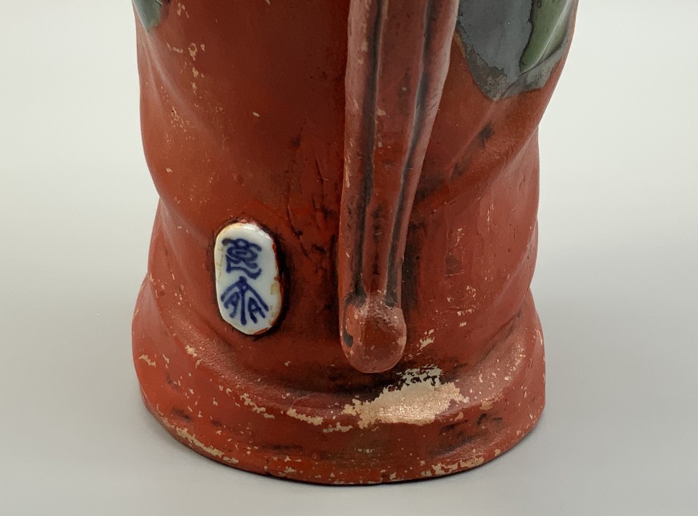 An antique Japanese Sumida Gawa lidded pottery jug sculpted in the form of a robed figure with red attire, green glaze drips, and a matching fitted lid. View IX