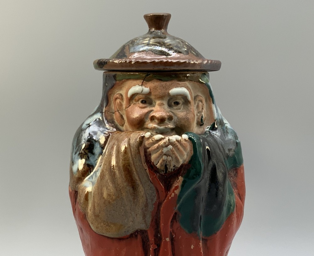 An antique Japanese Sumida Gawa lidded pottery jug sculpted in the form of a robed figure with red attire, green glaze drips, and a matching fitted lid. View XI