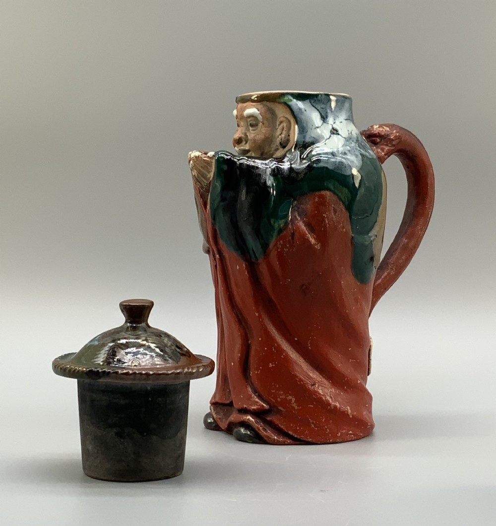 An antique Japanese Sumida Gawa lidded pottery jug sculpted in the form of a robed figure with red attire, green glaze drips, and a matching fitted lid. View XII