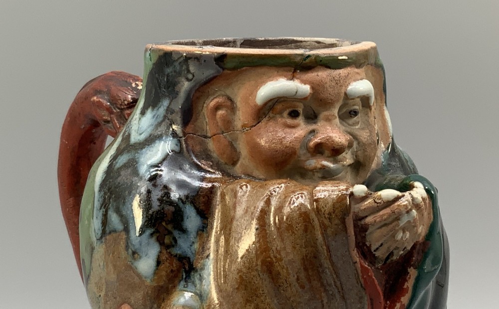 An antique Japanese Sumida Gawa lidded pottery jug sculpted in the form of a robed figure with red attire, green glaze drips, and a matching fitted lid. View XIII