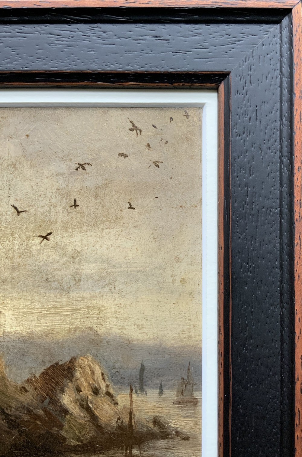A 19th-century miniature oil painting depicting a coastal cliff scene with a prominent rock stack, small boats, and birds in flight, set within a dark wooden frame. View IX