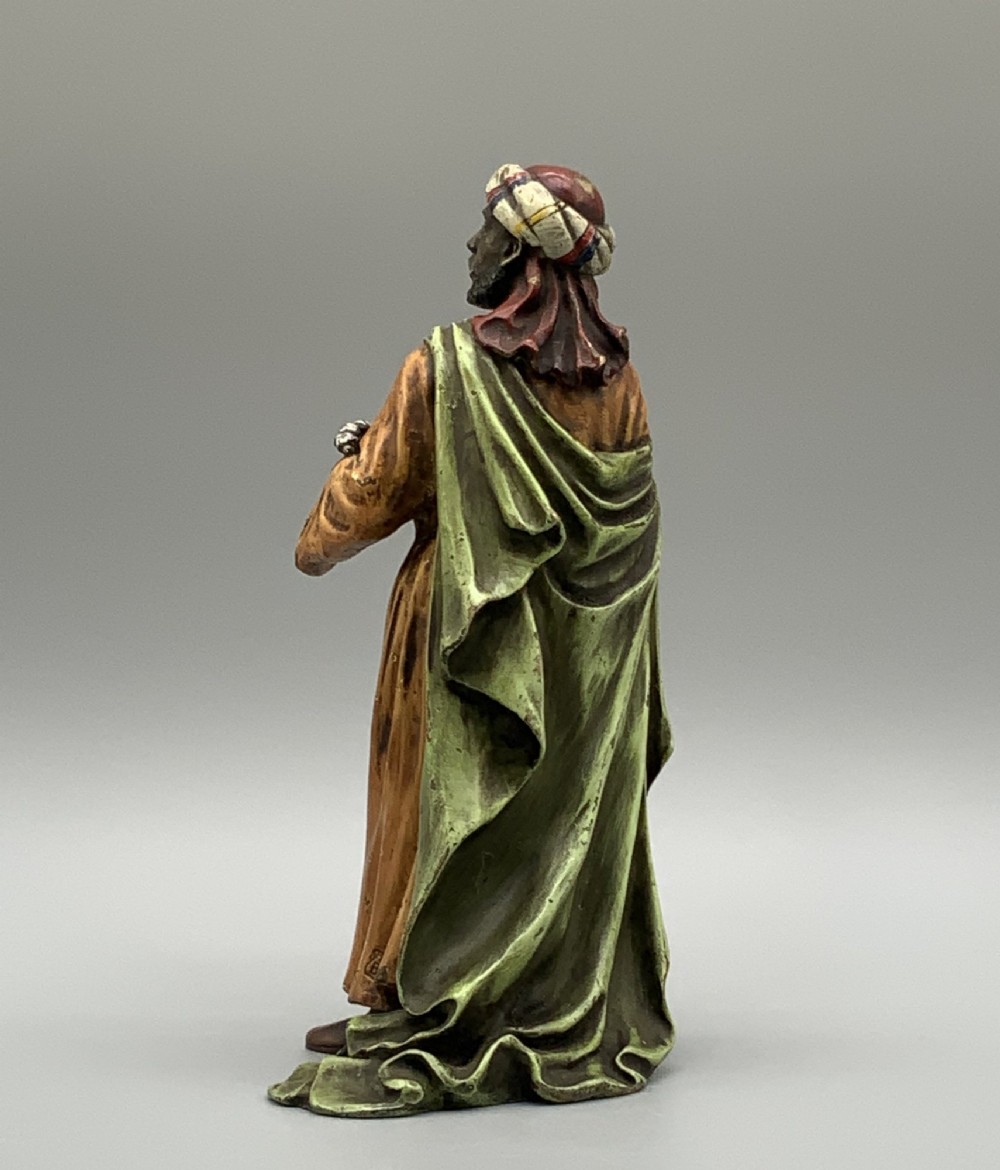 A cold-painted bronze Orientalist figure wearing a turban and ochre robe, standing next to a small table displaying wares. View V