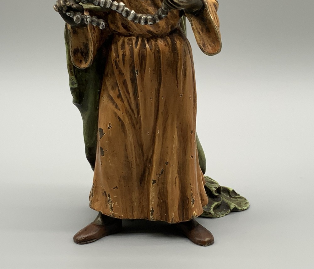 A cold-painted bronze Orientalist figure wearing a turban and ochre robe, standing next to a small table displaying wares. View X