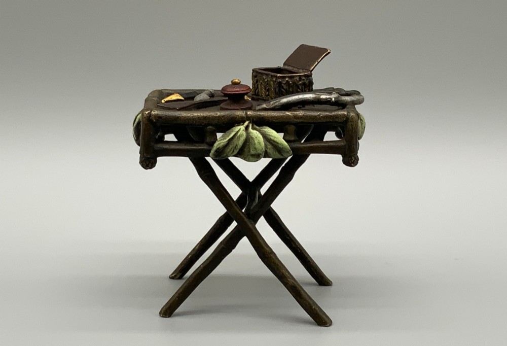 A cold-painted bronze Orientalist figure wearing a turban and ochre robe, standing next to a small table displaying wares. View XI