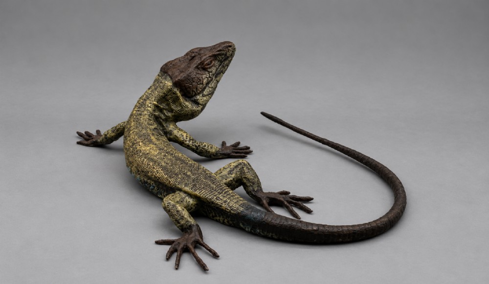 An antique cold-painted bronze sculpture depicting a realistic lizard with textured yellow and brown skin, blue accents, and a long curved tail. View V