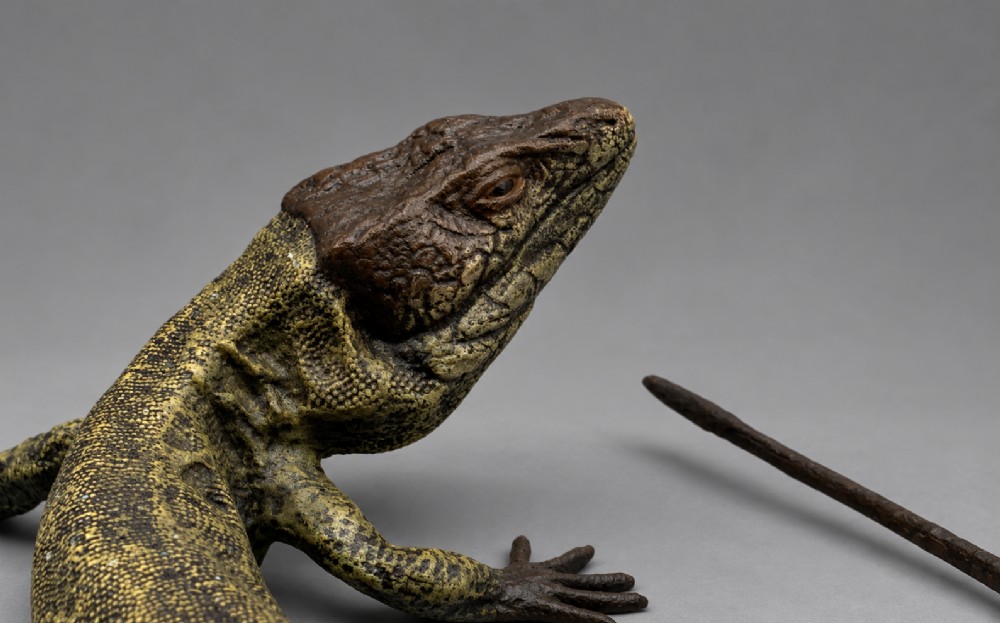 An antique cold-painted bronze sculpture depicting a realistic lizard with textured yellow and brown skin, blue accents, and a long curved tail. View VI