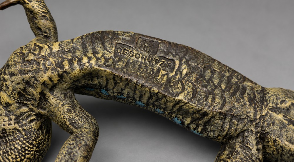 An antique cold-painted bronze sculpture depicting a realistic lizard with textured yellow and brown skin, blue accents, and a long curved tail. View X