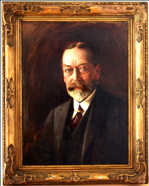 fig 1. A formal half-length oil portrait painting of King George V wearing a dark suit against a shaded brown background.