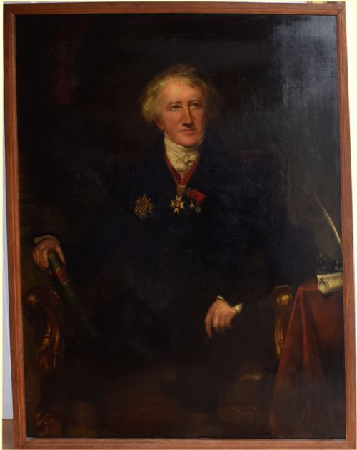 fig 6. An antique oil painting on canvas depicting a seated gentleman with white hair wearing a dark coat decorated with medals, holding a green book beside a red-draped table.
