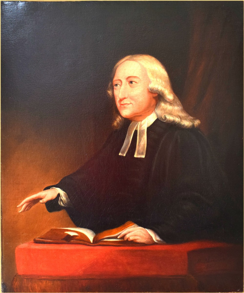 A Georgian oil portrait depicting John Wesley seated at a red cushion with an open book, wearing clerical robes and bands.