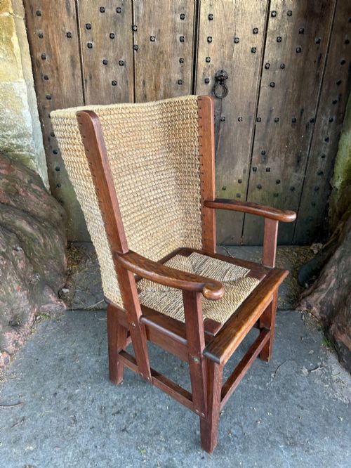 fig 1. An antique Scottish Orkney armchair featuring a dark oak wood frame, scrolled arms, a drop-in rush seat, and a tall woven straw backrest.