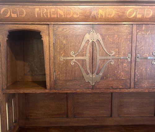 fig 2. A solid oak Arts and Crafts sideboard with an inscribed upper cornice, leaded glazed doors, open central niche, and long decorative iron hinges.
