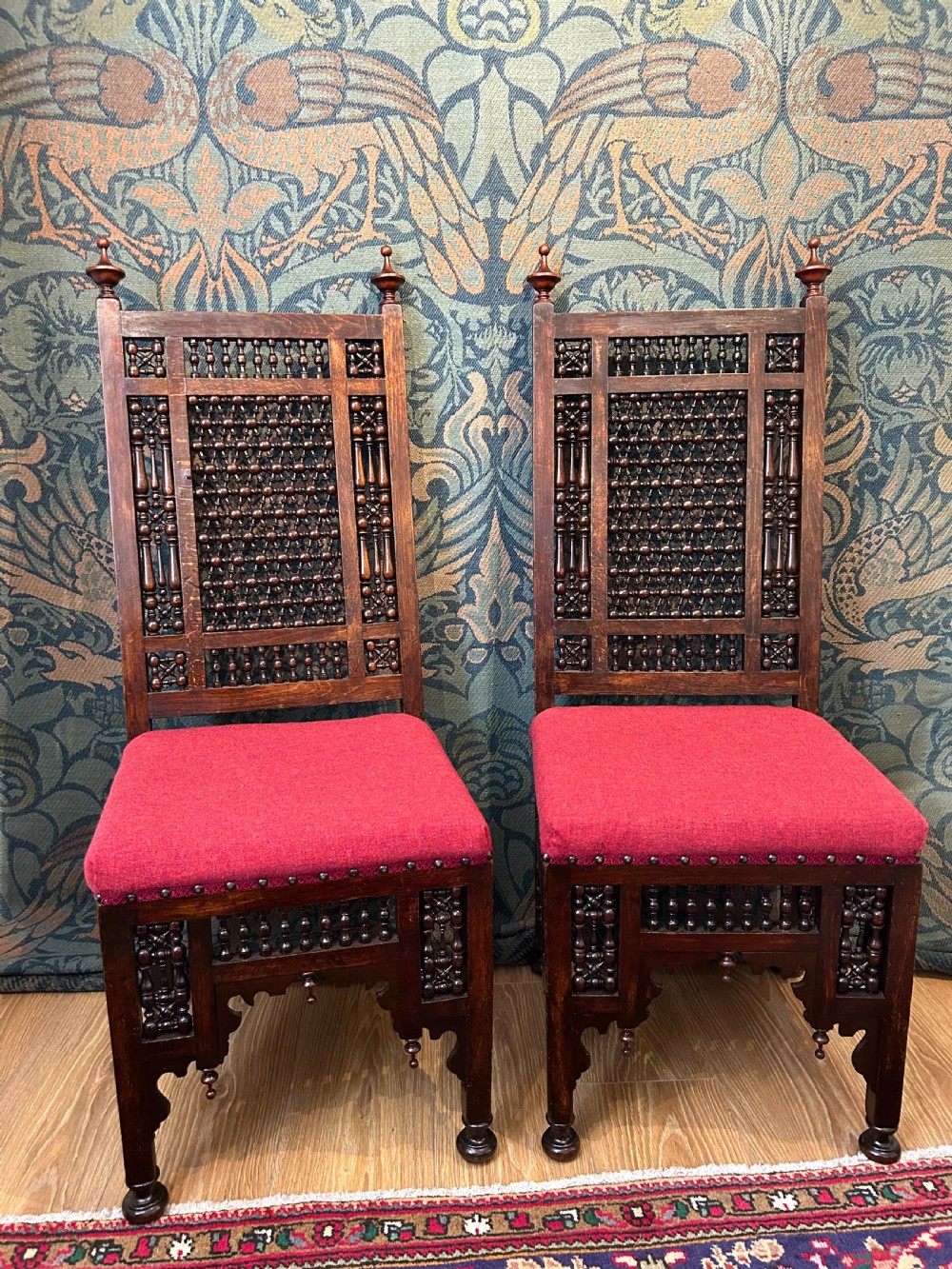 A pair of dark wood Cairene side chairs featuring turned bobbin mashrabiya latticework on the backrests and lower aprons, topped with corner finials and fitted with red wool upholstered seats.
