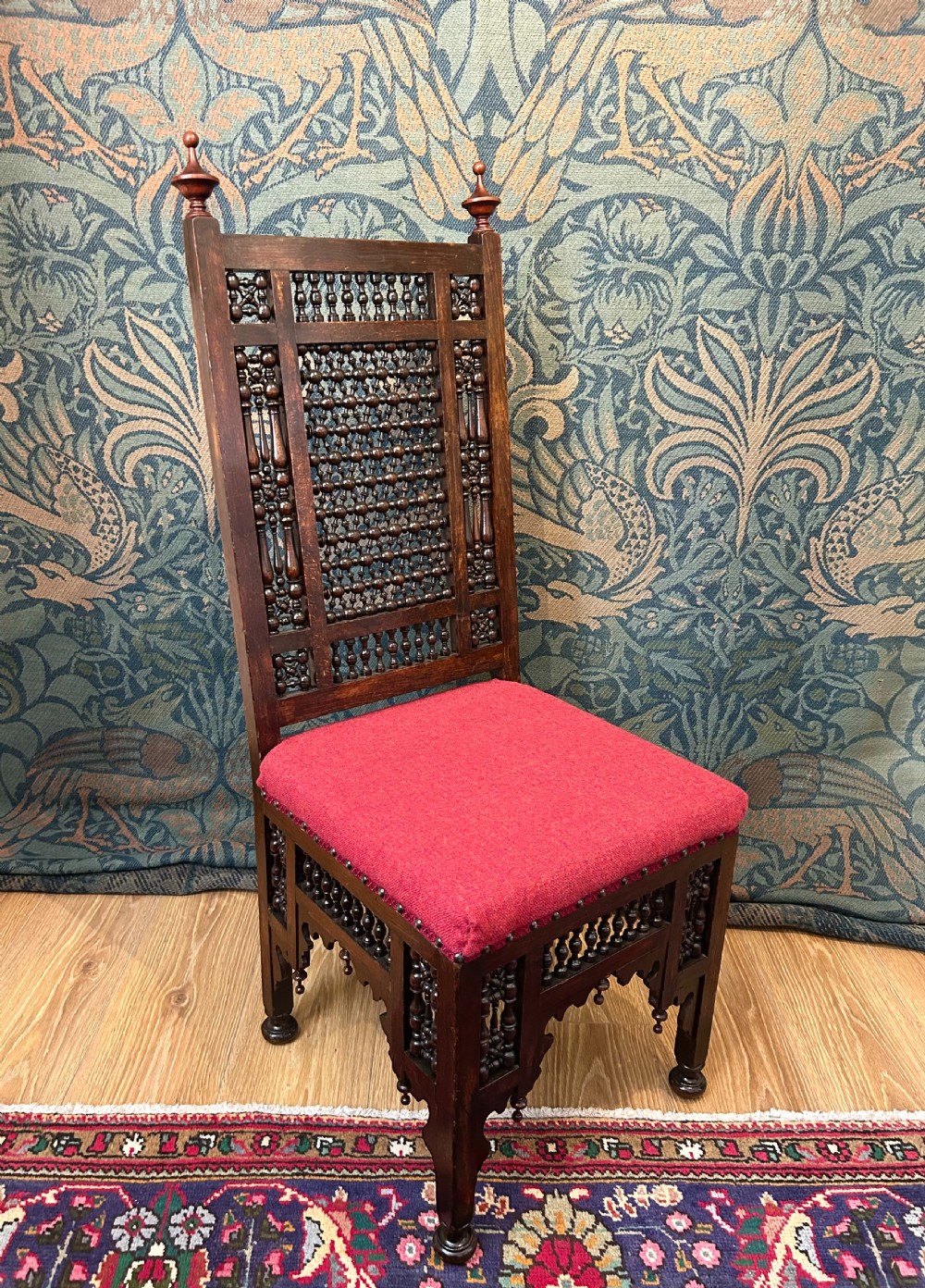 A pair of dark wood Cairene side chairs featuring turned bobbin mashrabiya latticework on the backrests and lower aprons, topped with corner finials and fitted with red wool upholstered seats. View VI