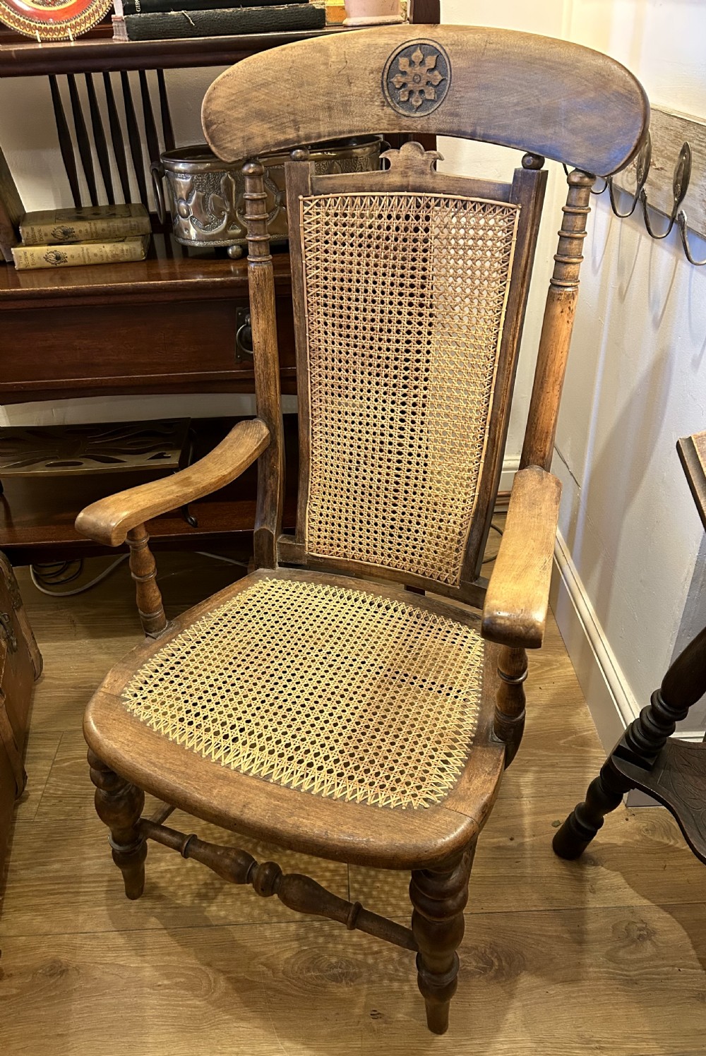 A rustic wooden armchair featuring a high back with a woven cane panel, a woven cane seat, curved armrests, and turned front legs with carved details on the top rail. View II