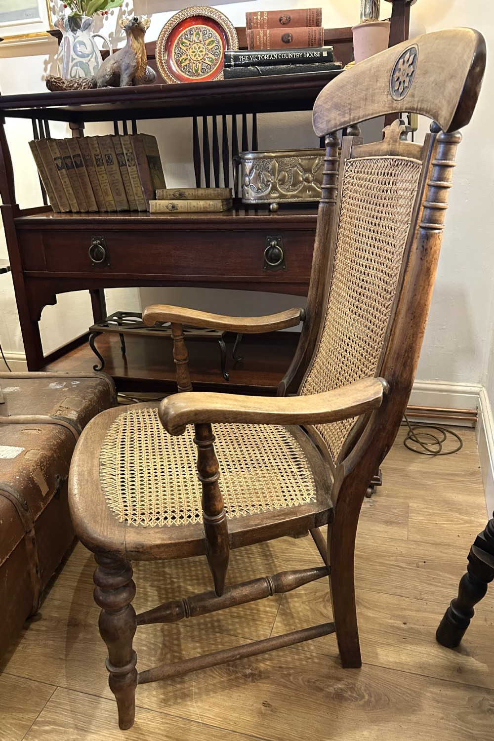 A rustic wooden armchair featuring a high back with a woven cane panel, a woven cane seat, curved armrests, and turned front legs with carved details on the top rail. View III