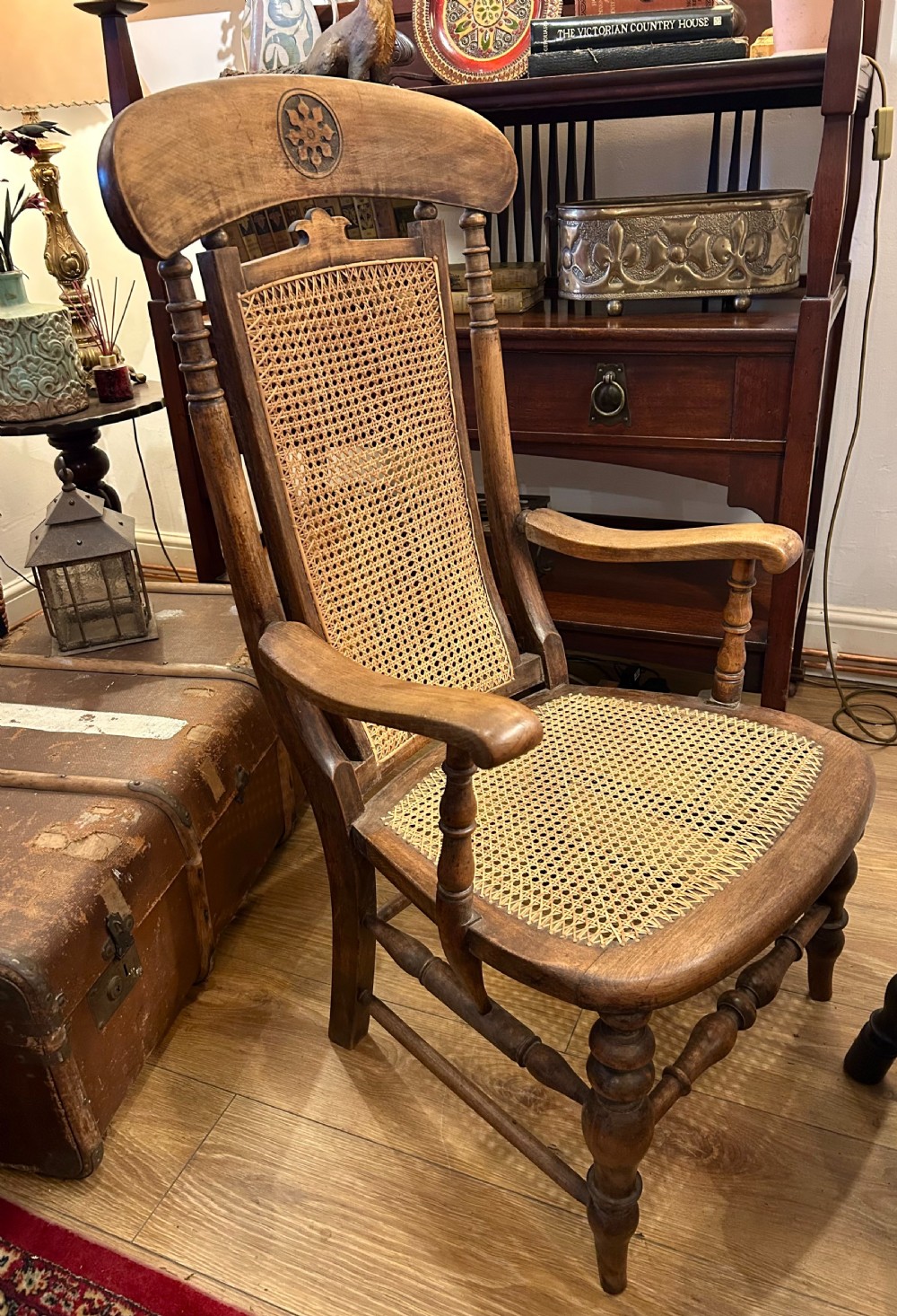A rustic wooden armchair featuring a high back with a woven cane panel, a woven cane seat, curved armrests, and turned front legs with carved details on the top rail. View V