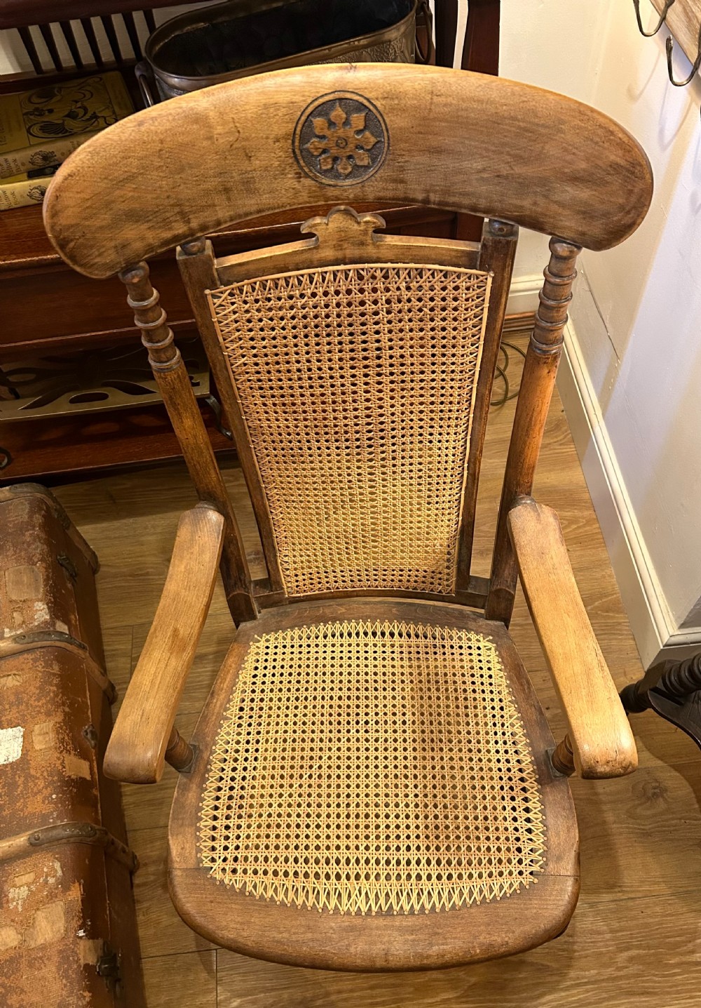 A rustic wooden armchair featuring a high back with a woven cane panel, a woven cane seat, curved armrests, and turned front legs with carved details on the top rail. View VII