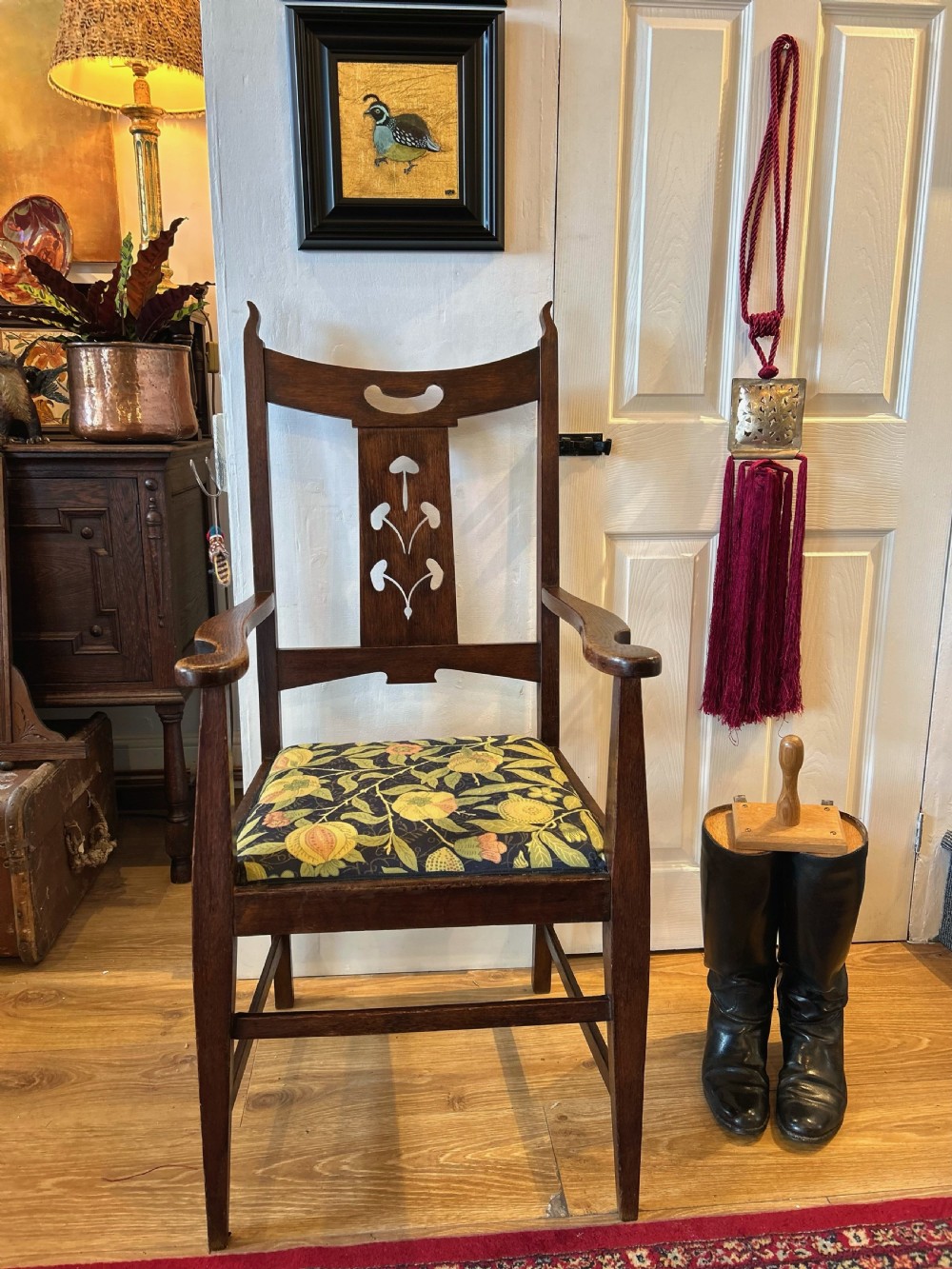 A dark oak Arts and Crafts armchair featuring a high back with a central floral inlaid splat, shaped armrests, and a botanical patterned upholstered seat. View III