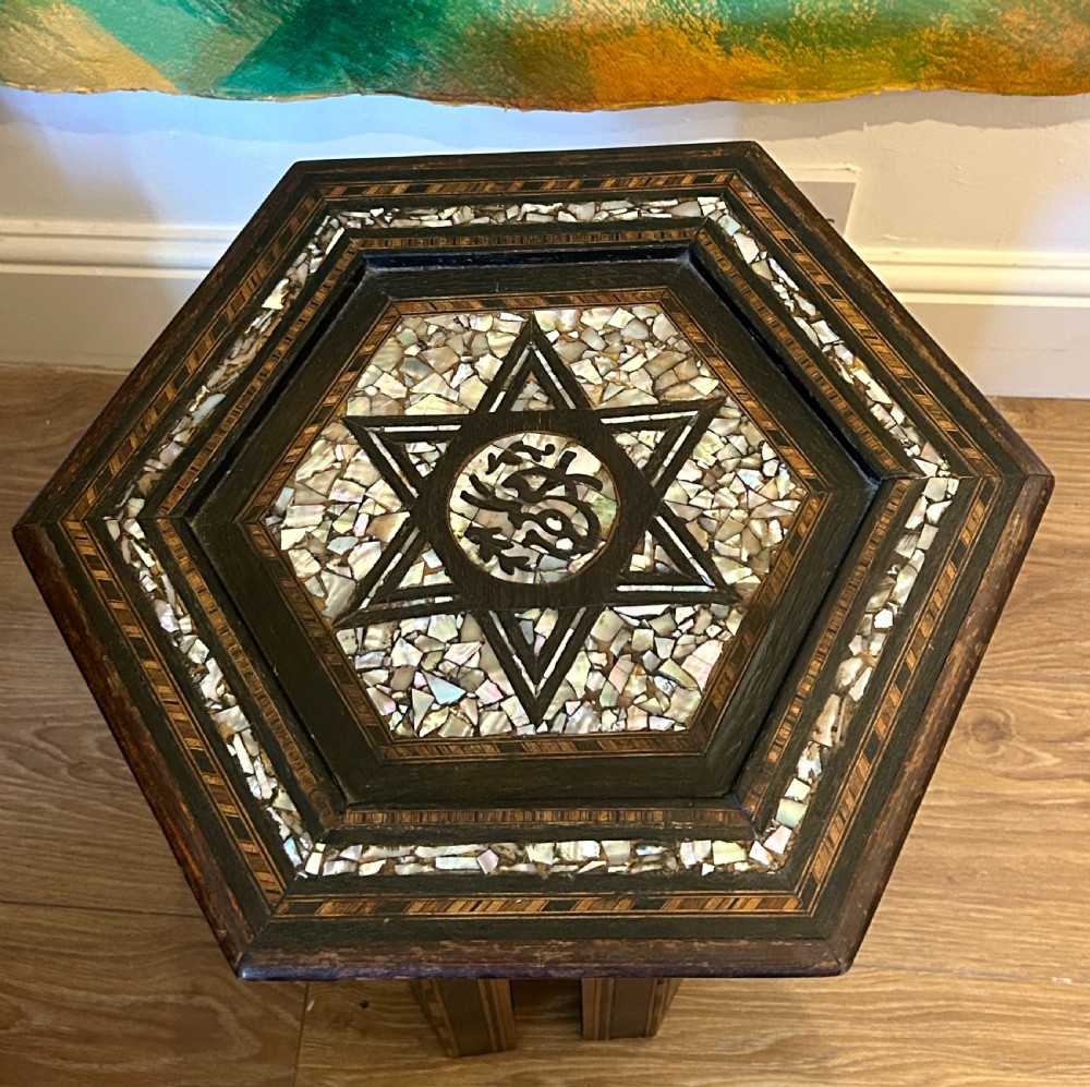 A hexagonal dark wood side table featuring intricate Mother-of-Pearl geometric inlays, a central calligraphic star motif, and arched cutout legs. View VI