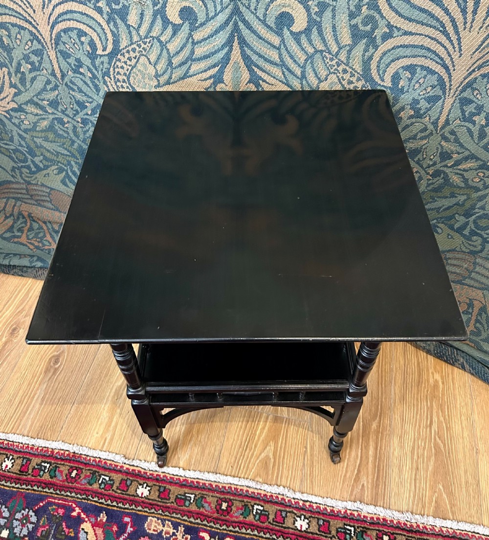 An Aesthetic Movement ebonised wooden side table featuring turned legs, a lower shelf with spindle railing, arched corner brackets, and brass castors. View VII