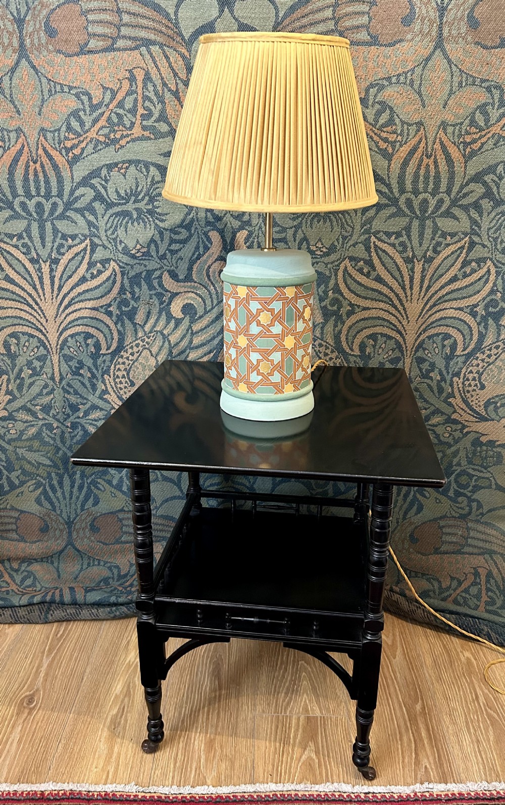 An Aesthetic Movement ebonised wooden side table featuring turned legs, a lower shelf with spindle railing, arched corner brackets, and brass castors. View VIII