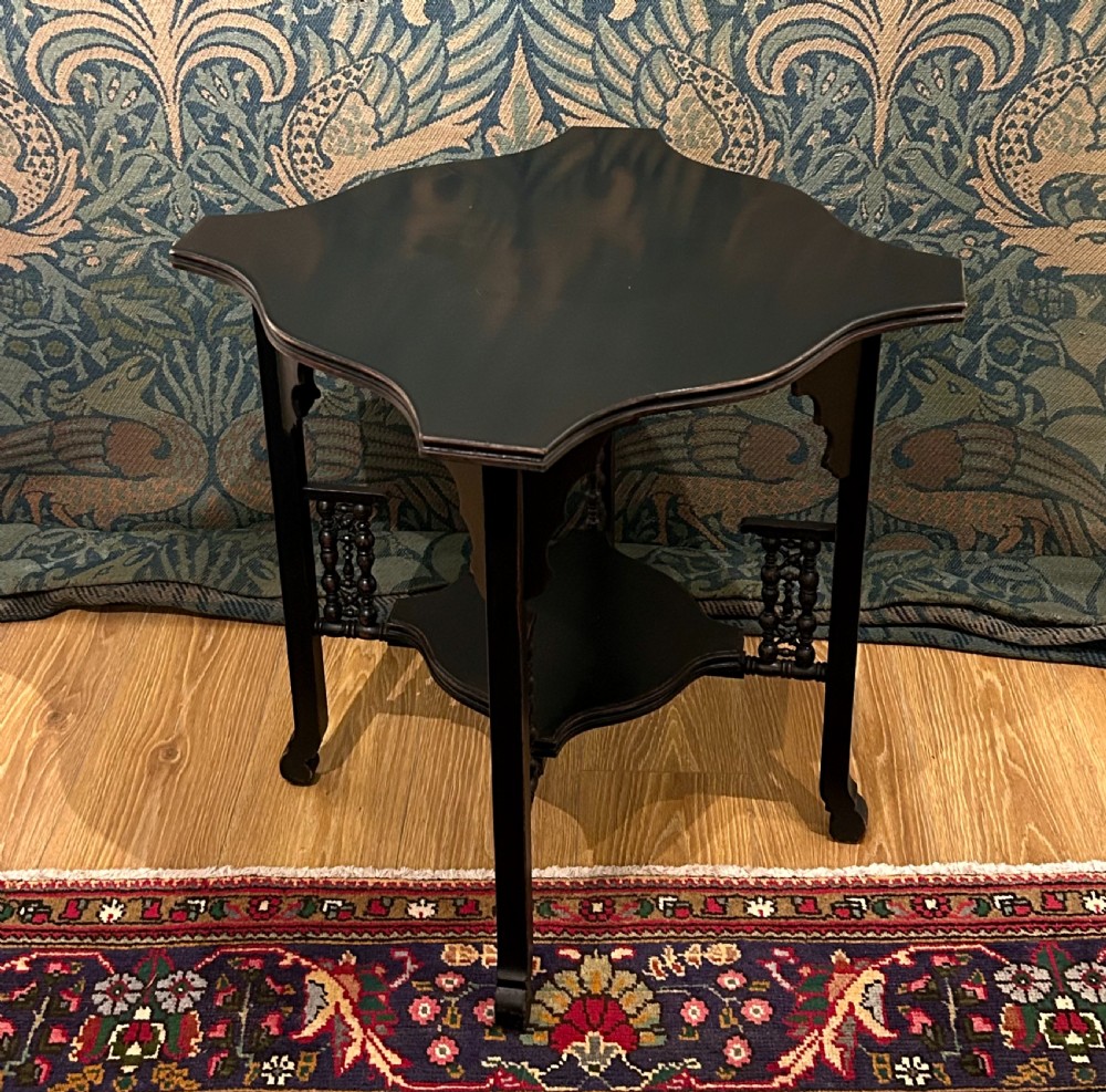 An ebonised wooden Anglo-Moorish occasional table featuring a shaped top, lower tier, and turned spindle gallery details.