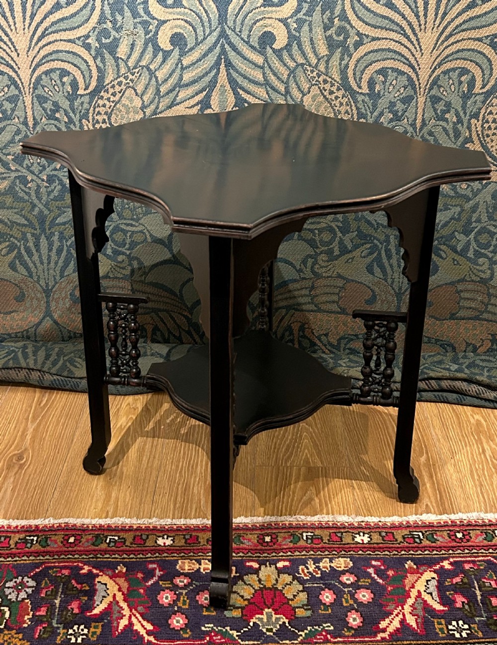 An ebonised wooden Anglo-Moorish occasional table featuring a shaped top, lower tier, and turned spindle gallery details. View II