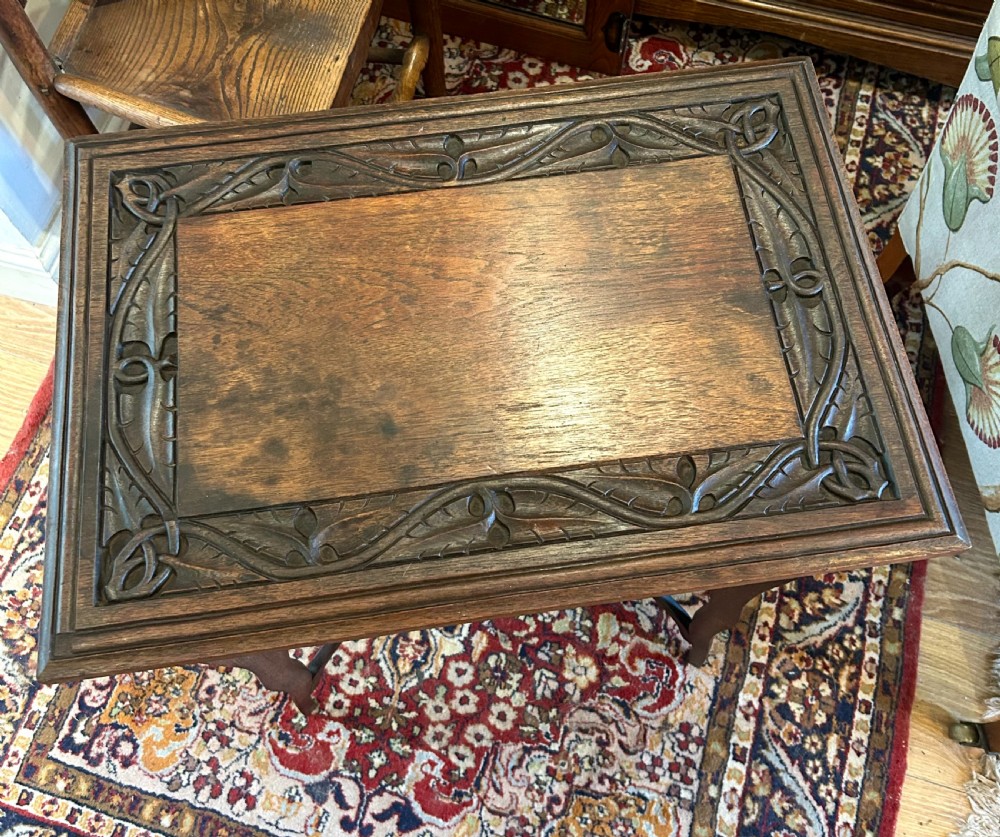 A warm brown oak occasional table with a relief-carved botanical border on the tabletop, slender curved legs, and an integrated lower rectangular tier. View IV