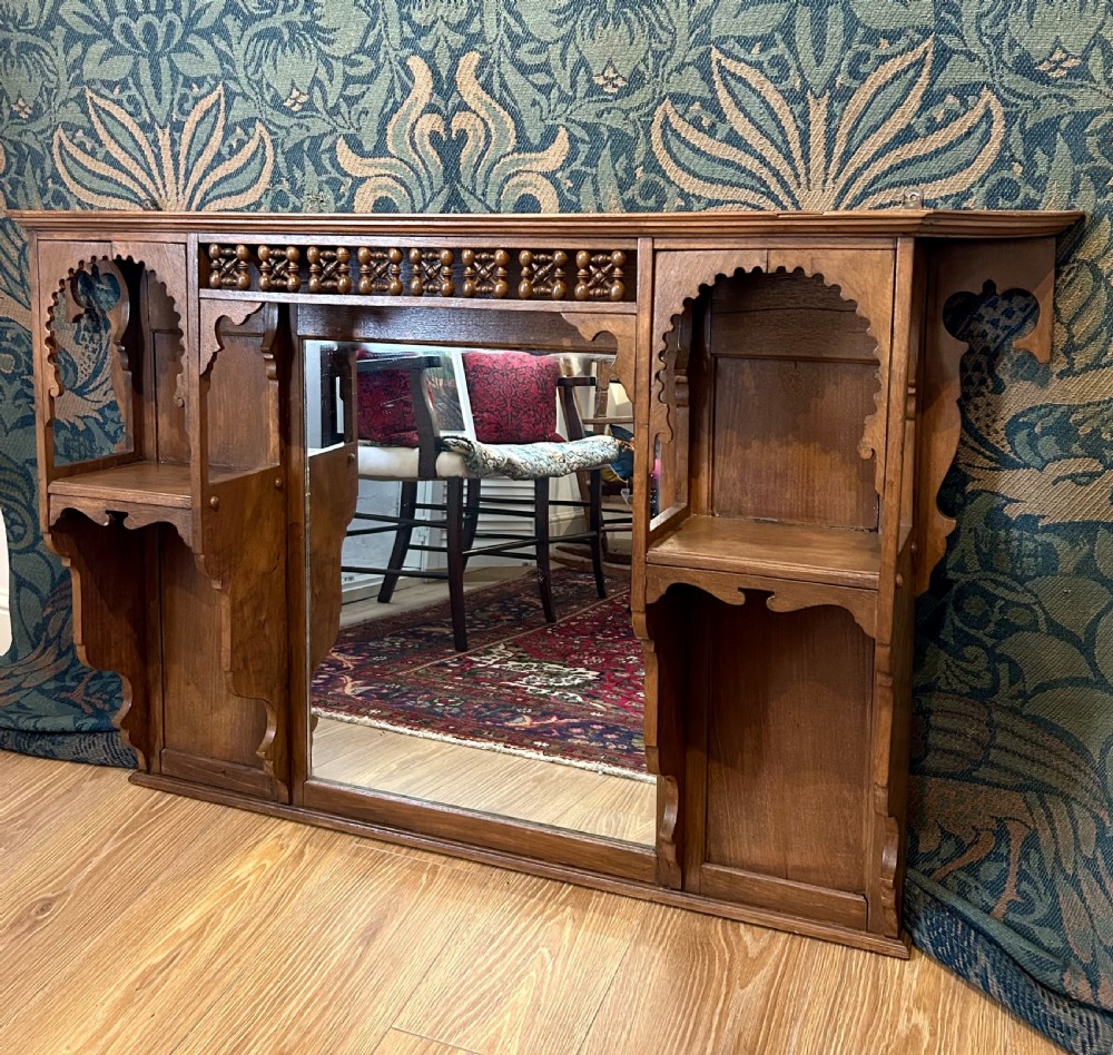 A carved wooden Moorish style overmantel mirror with a central glass panel, horseshoe arch side shelves, and a top turned spindle gallery. View II