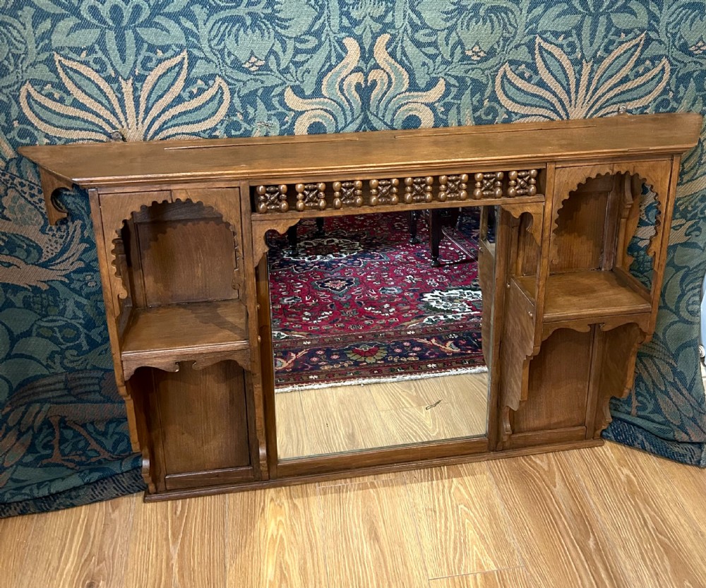 A carved wooden Moorish style overmantel mirror with a central glass panel, horseshoe arch side shelves, and a top turned spindle gallery. View III