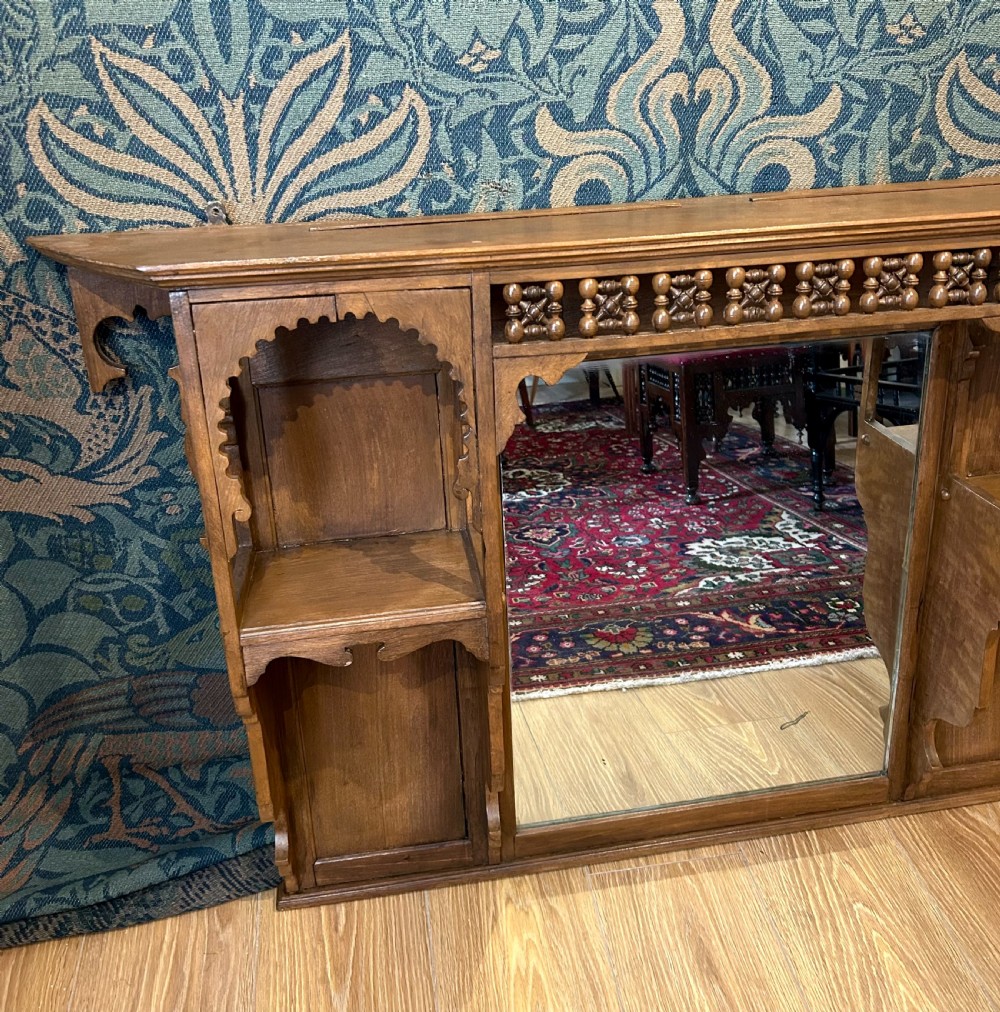 A carved wooden Moorish style overmantel mirror with a central glass panel, horseshoe arch side shelves, and a top turned spindle gallery. View IV