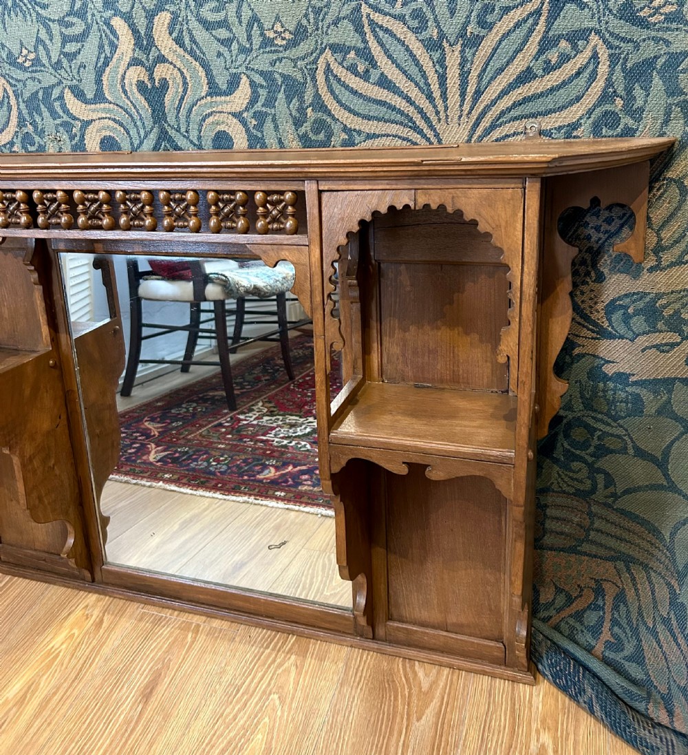 A carved wooden Moorish style overmantel mirror with a central glass panel, horseshoe arch side shelves, and a top turned spindle gallery. View V