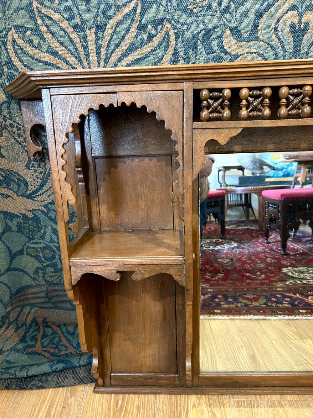 A carved wooden Moorish style overmantel mirror with a central glass panel, horseshoe arch side shelves, and a top turned spindle gallery. View VI