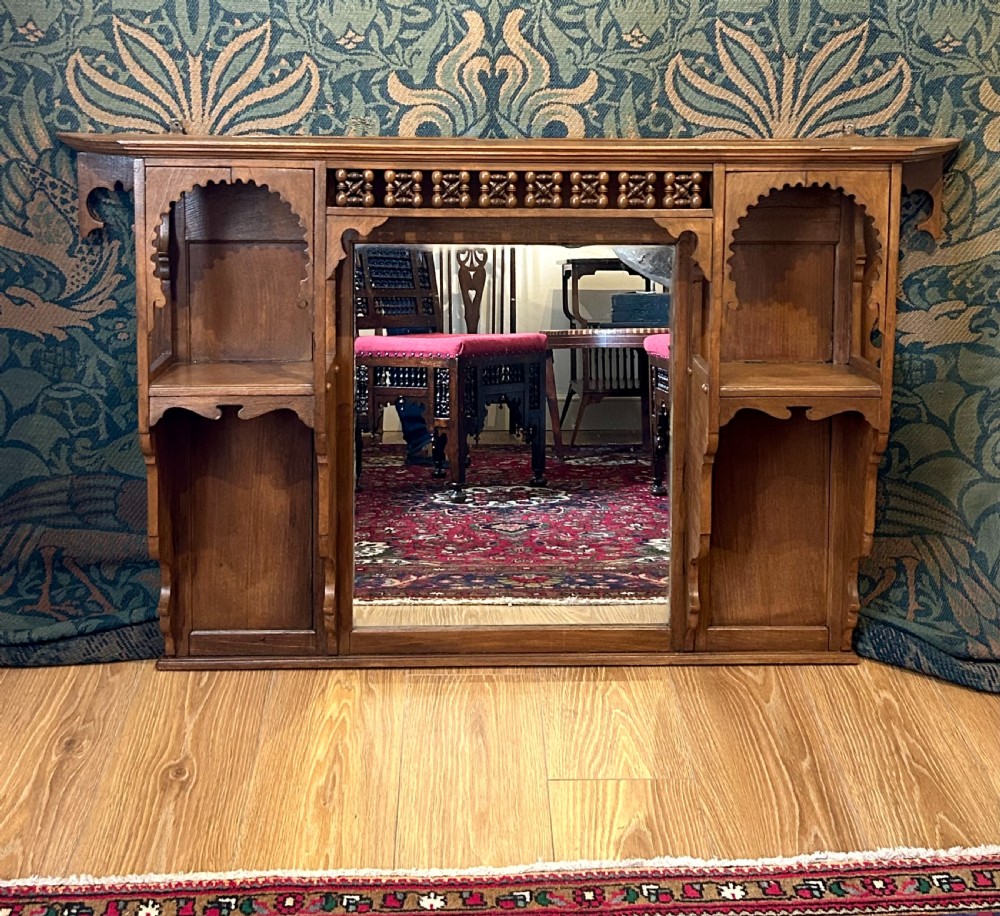 A carved wooden Moorish style overmantel mirror with a central glass panel, horseshoe arch side shelves, and a top turned spindle gallery. View VIII