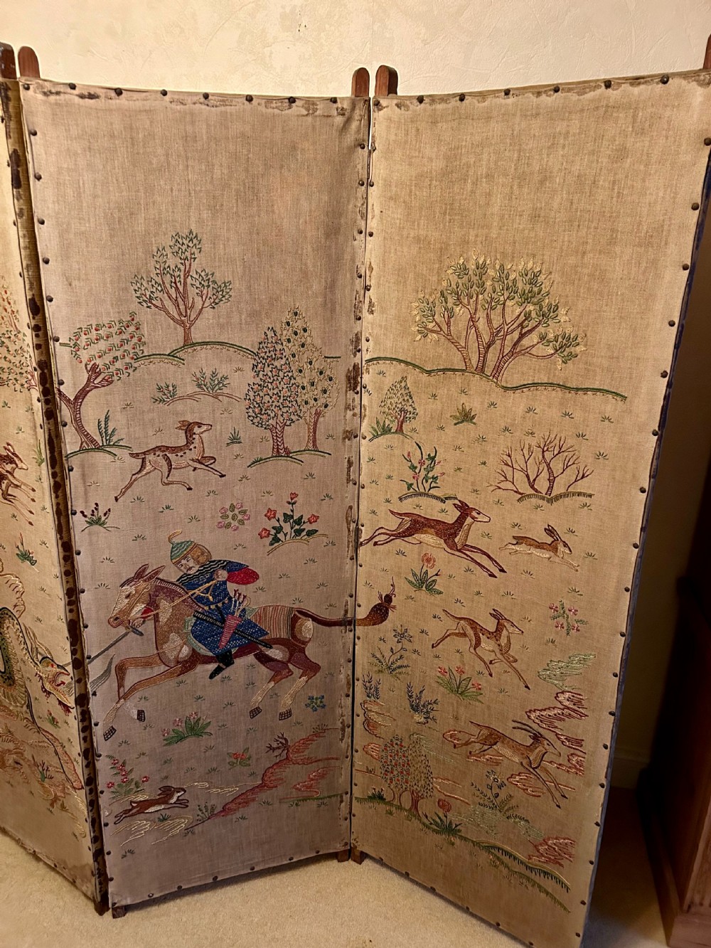 A three-panel folding room screen constructed with natural beige linen panels embroidered with Persian-style equestrian and mythological creature motifs, secured with brass tacks. View III