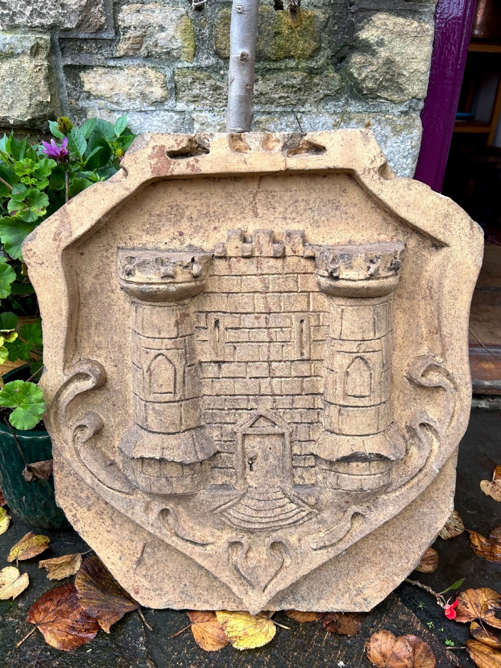 A carved buff stone armorial shield plaque featuring a relief depiction of a twin-towered castle gate with scrolled side details.