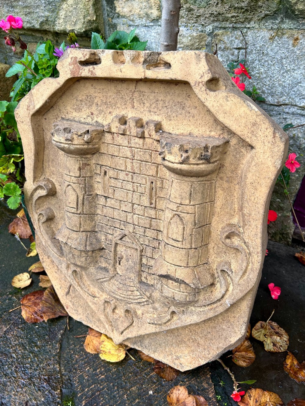 A carved buff stone armorial shield plaque featuring a relief depiction of a twin-towered castle gate with scrolled side details. View II
