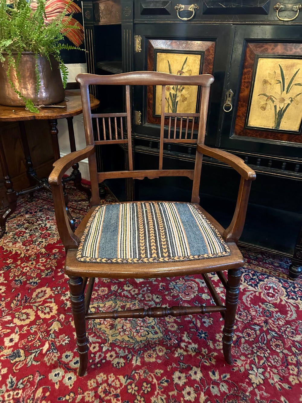 An Aesthetic Movement timber armchair with turned legs, spindle back details, curved armrests, and a striped woven fabric seat.