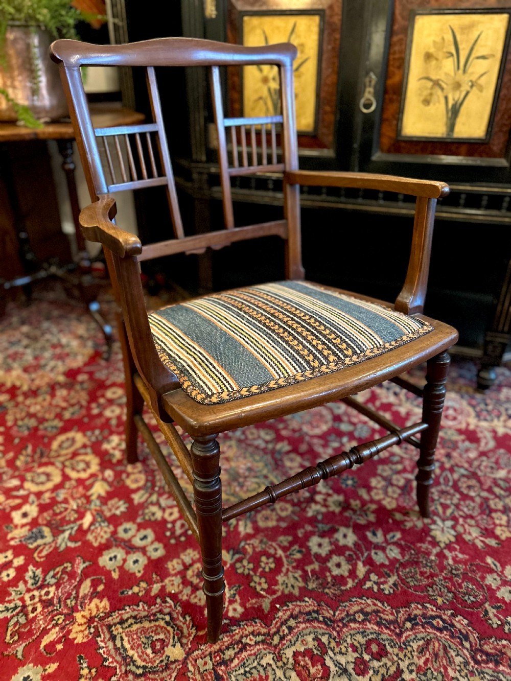 An Aesthetic Movement timber armchair with turned legs, spindle back details, curved armrests, and a striped woven fabric seat. View II