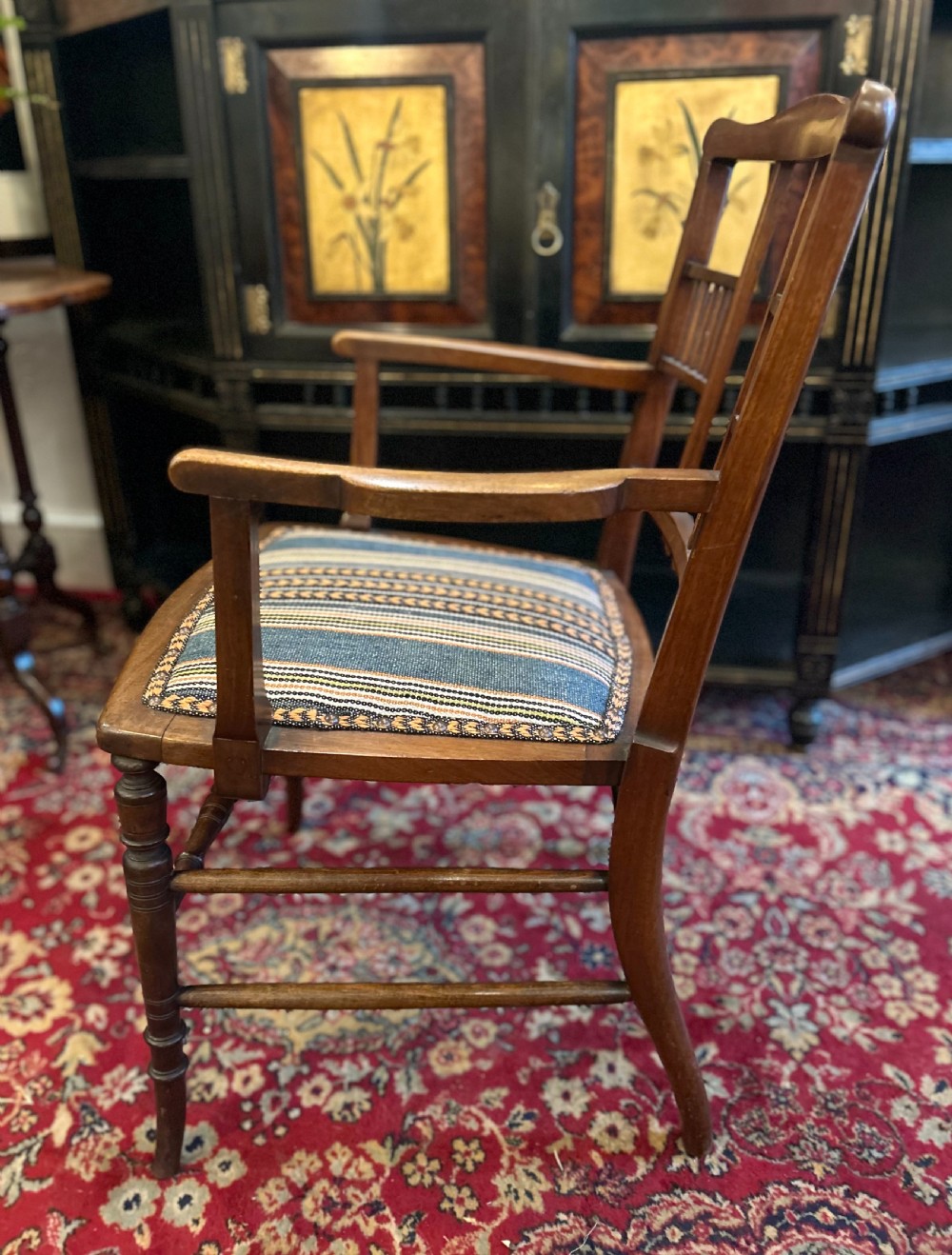 An Aesthetic Movement timber armchair with turned legs, spindle back details, curved armrests, and a striped woven fabric seat. View V