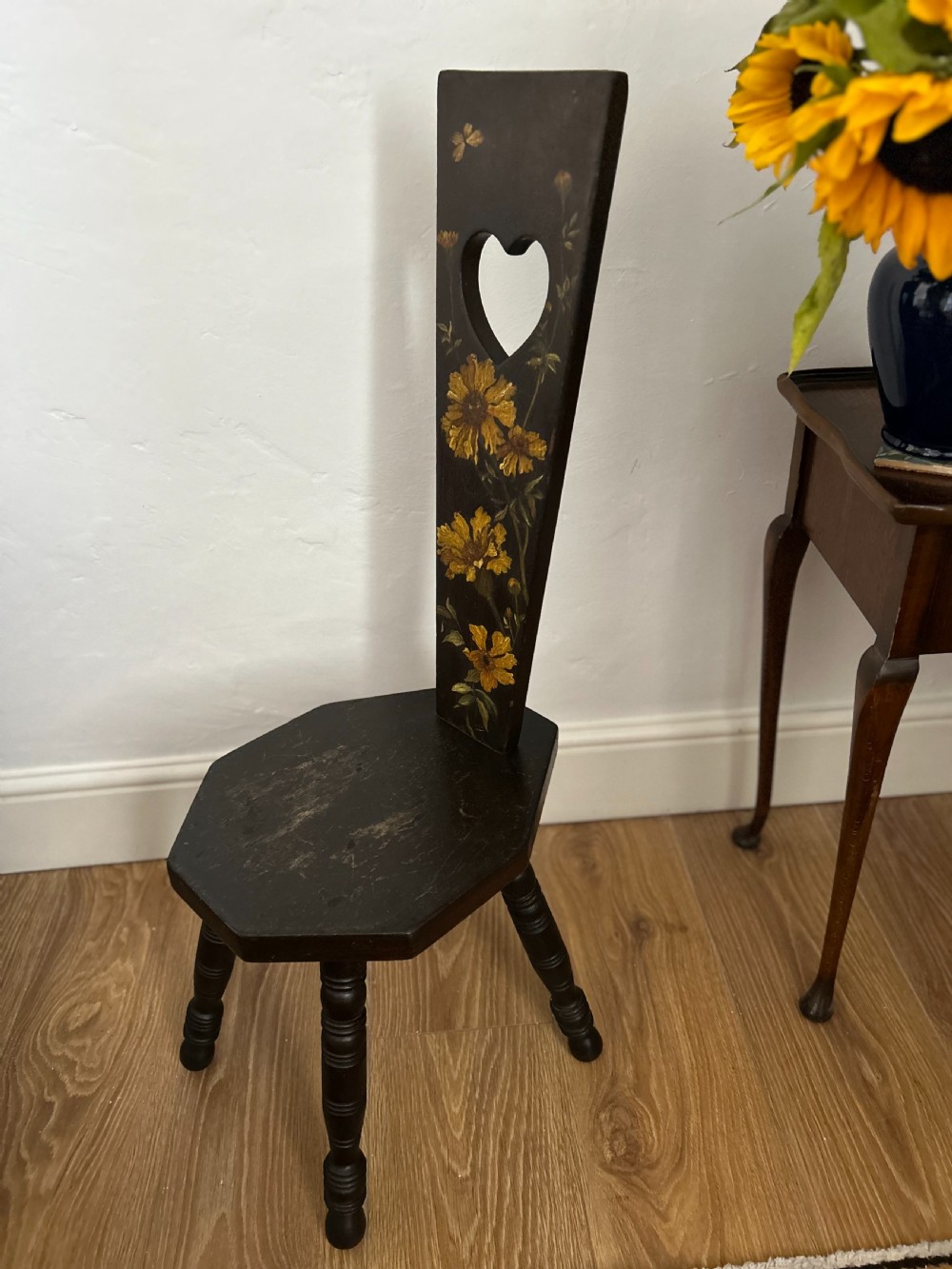 A dark wood Welsh spinning chair featuring a tall narrow backrest decorated with hand-painted yellow flowers and a heart cutout above a hexagonal seat and turned legs. View III