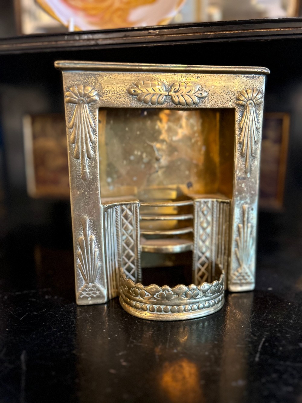 A Victorian brass tradesmans sample fireplace featuring embossed foliage details, a central grate, and a curved fender. View II