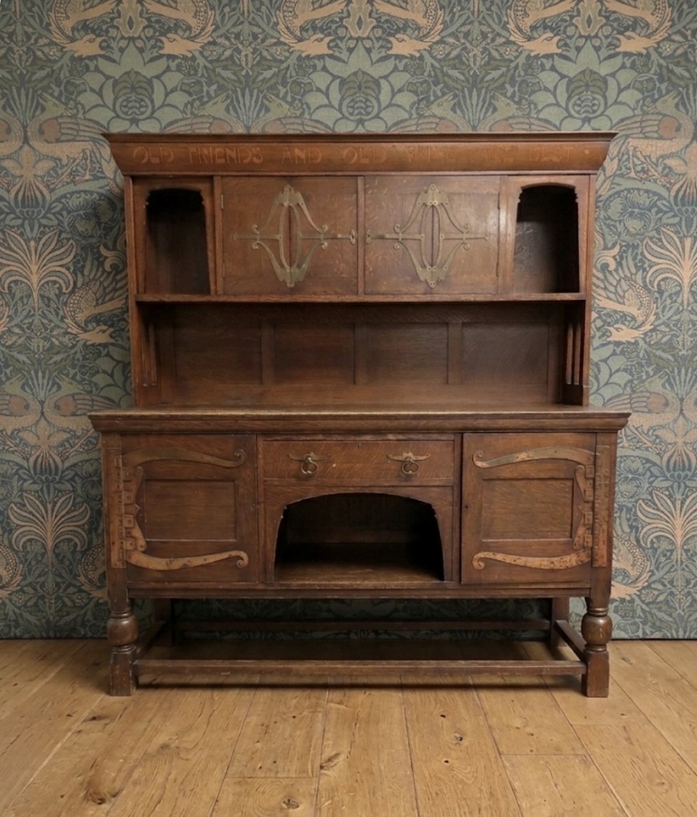 A solid oak Arts and Crafts sideboard with an inscribed upper cornice, leaded glazed doors, open central niche, and long decorative iron hinges. View II