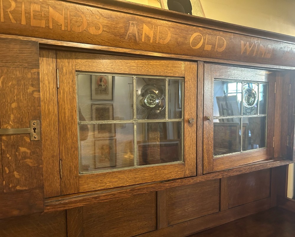 A solid oak Arts and Crafts sideboard with an inscribed upper cornice, leaded glazed doors, open central niche, and long decorative iron hinges. View V