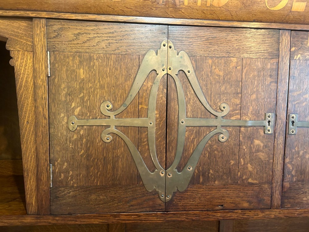 A solid oak Arts and Crafts sideboard with an inscribed upper cornice, leaded glazed doors, open central niche, and long decorative iron hinges. View VI