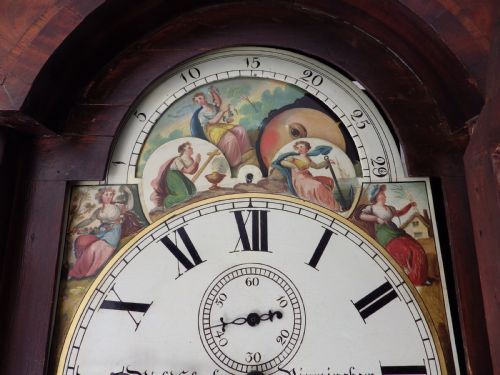 fig 2. An antique flame mahogany longcase clock featuring a painted dial, swan-neck pediment with brass finials, and spirally turned column detailing.