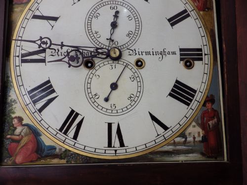 fig 3. An antique flame mahogany longcase clock featuring a painted dial, swan-neck pediment with brass finials, and spirally turned column detailing.